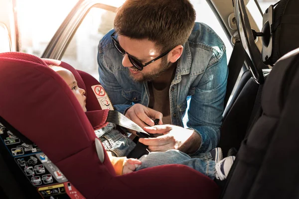 Отец закрепите его ребенка в сиденье автомобиля — стоковое фото